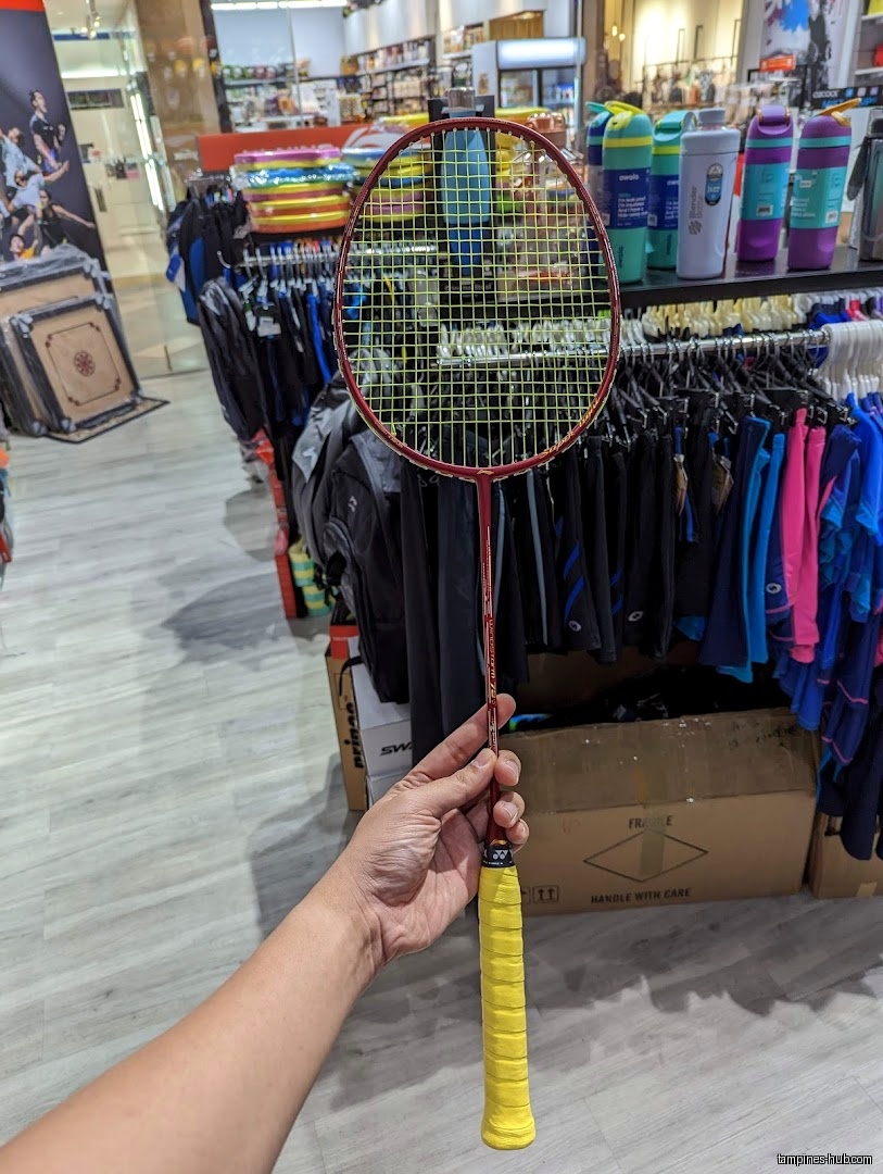 A hand holds a badminton racket inside the Flymax shop.