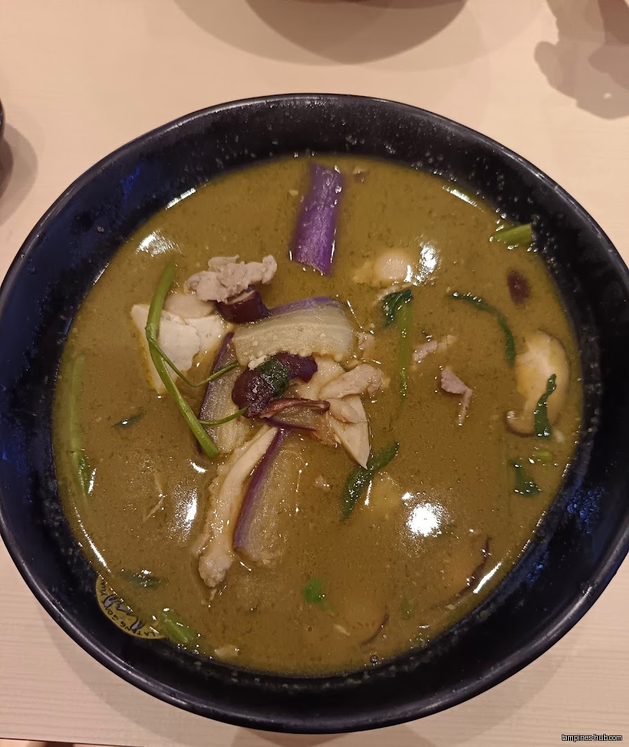 A bowl of green curry with eggplant and meat is shown.
