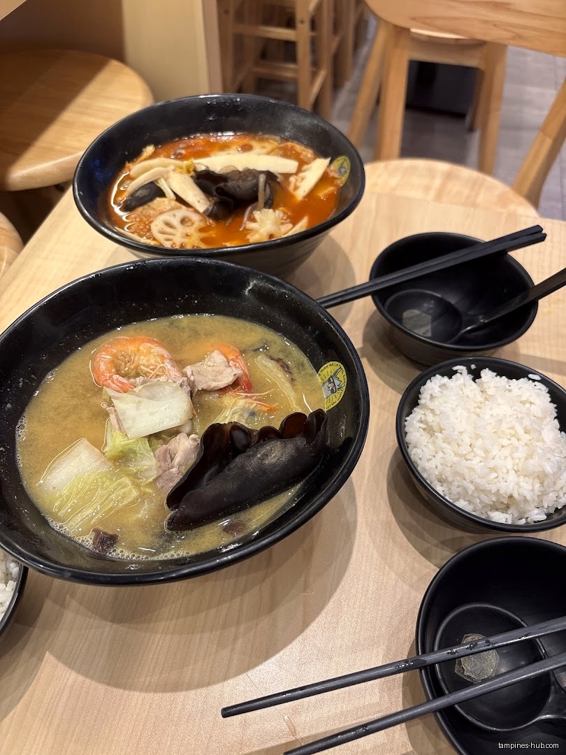 Two bowls of Ma La Tang soup with rice and utensils on a table.