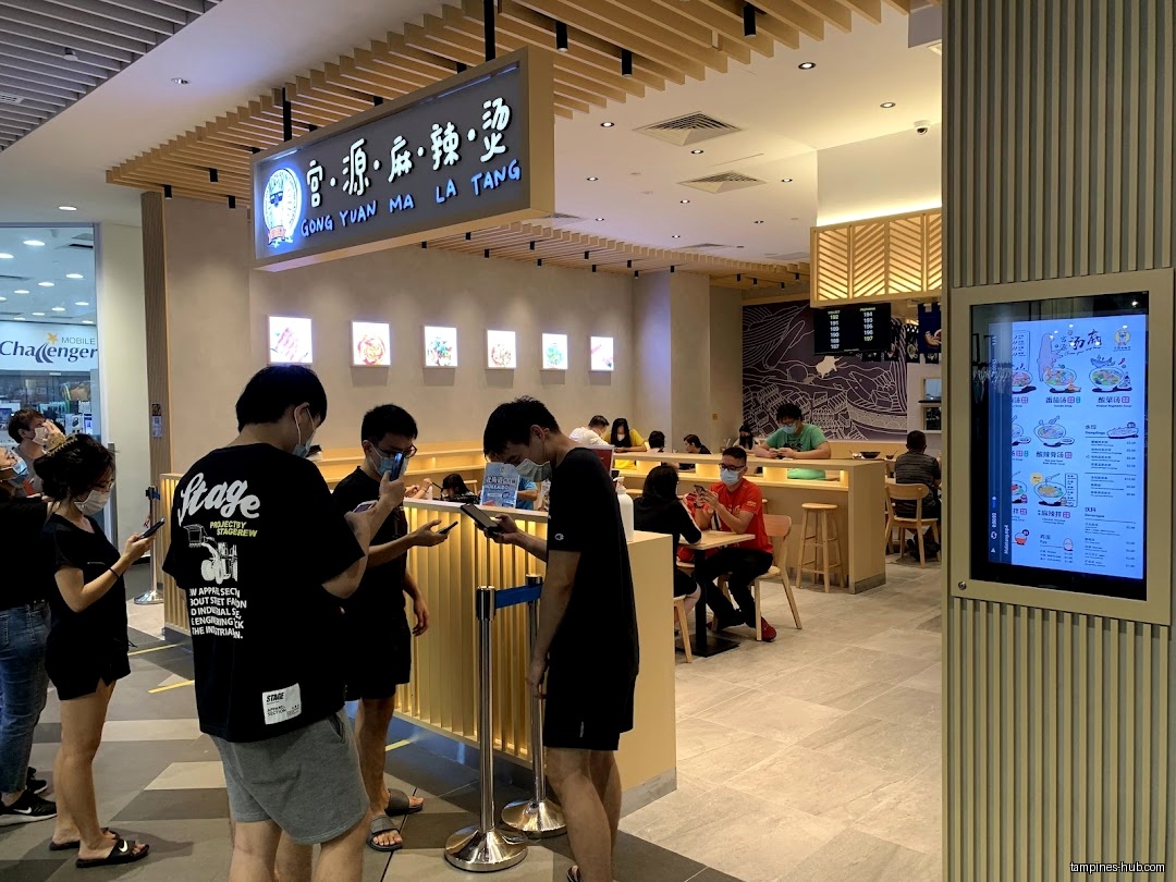 Customers queue at Gong Yuan Ma La Tang, some looking at their phones.