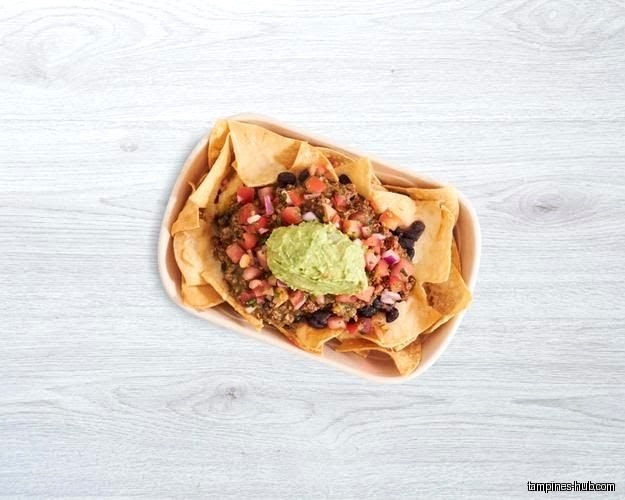 Overhead shot of nachos with guacamole, tomatoes, and black beans in a bowl.