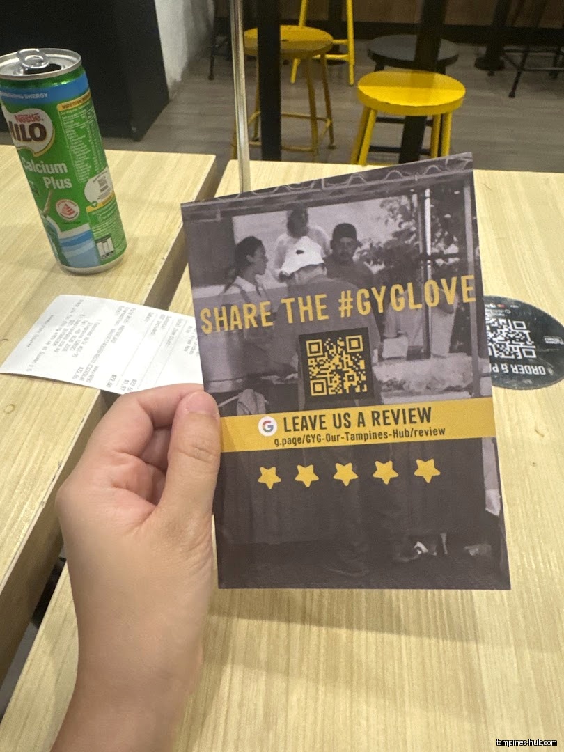 A hand holds a Guzman y Gomez review card on a table.