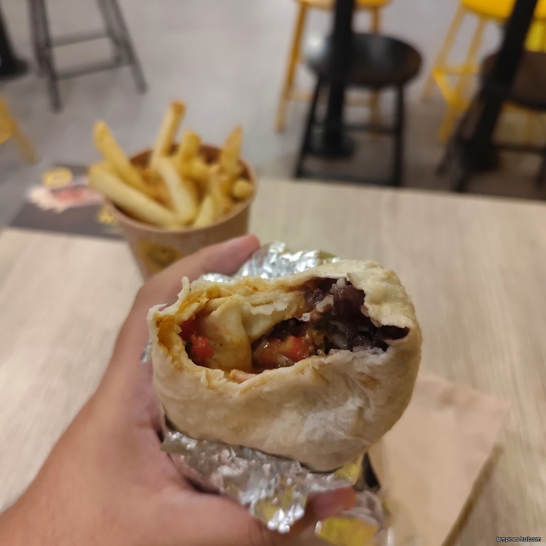 A hand holds a half-eaten burrito with fries in the background.