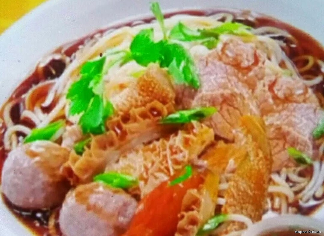 A bowl of Hainan beef noodle soup with meat and vegetables.