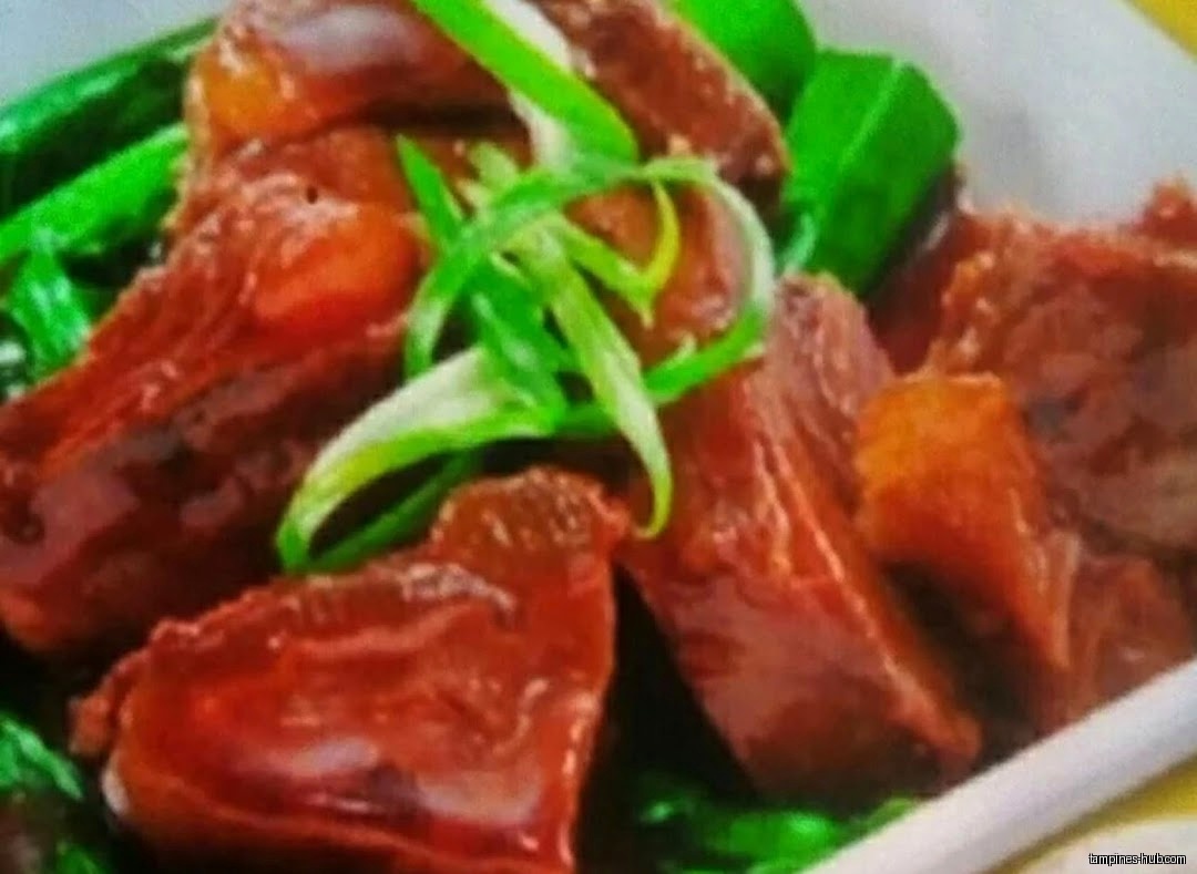 Close-up of braised beef with green vegetables and scallion garnish.