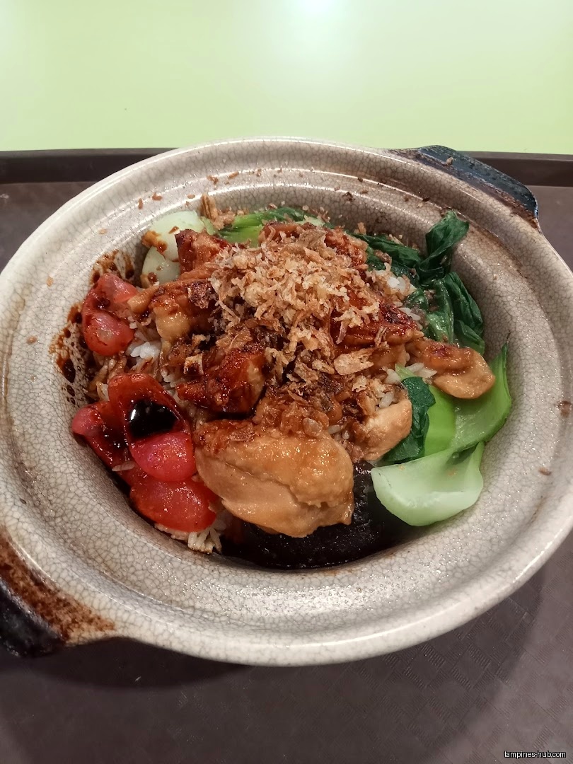 A close-up shot of claypot rice with chicken, vegetables, and fried onions.