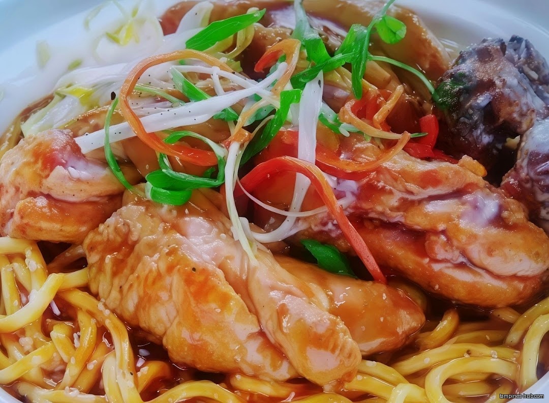 Close-up of Hainan beef noodle dish with colorful garnish and sauce.