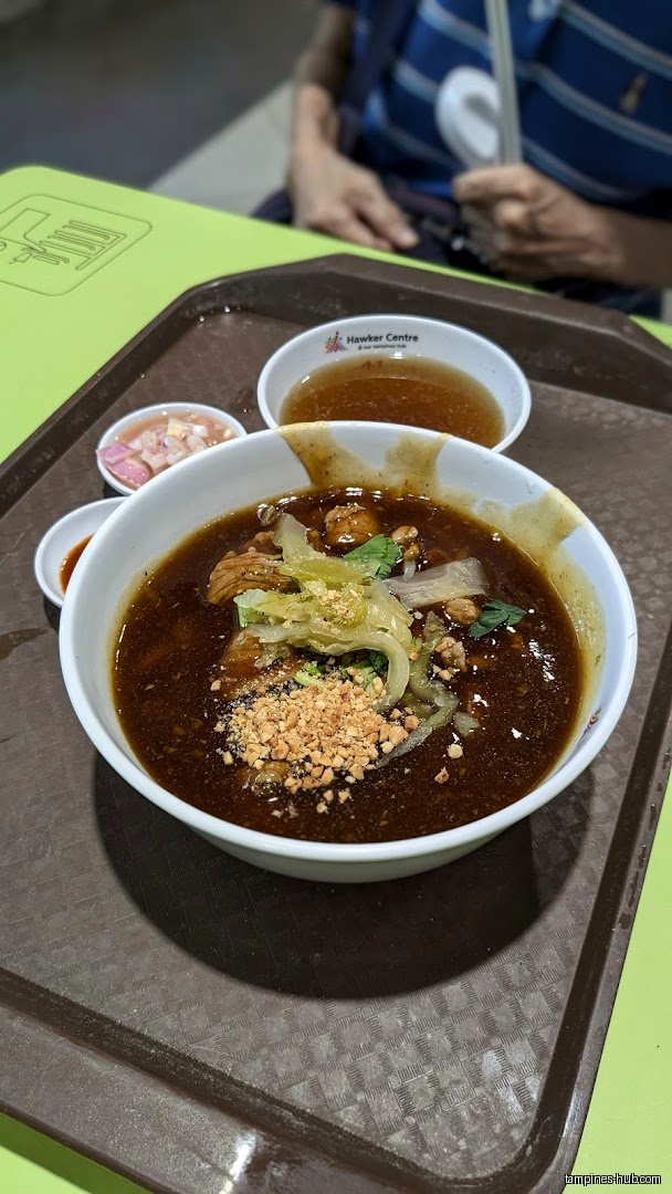 A bowl of Hainan beef noodle soup with peanuts and side dishes.