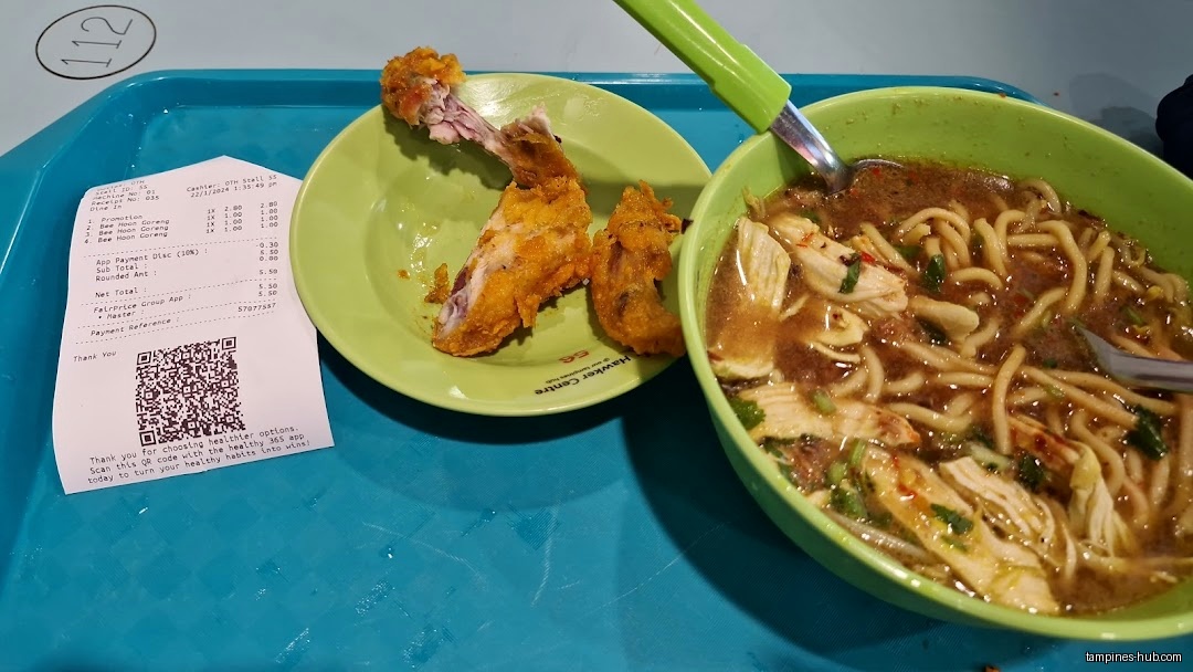 A bowl of noodles, fried chicken remains, and a receipt on a tray.