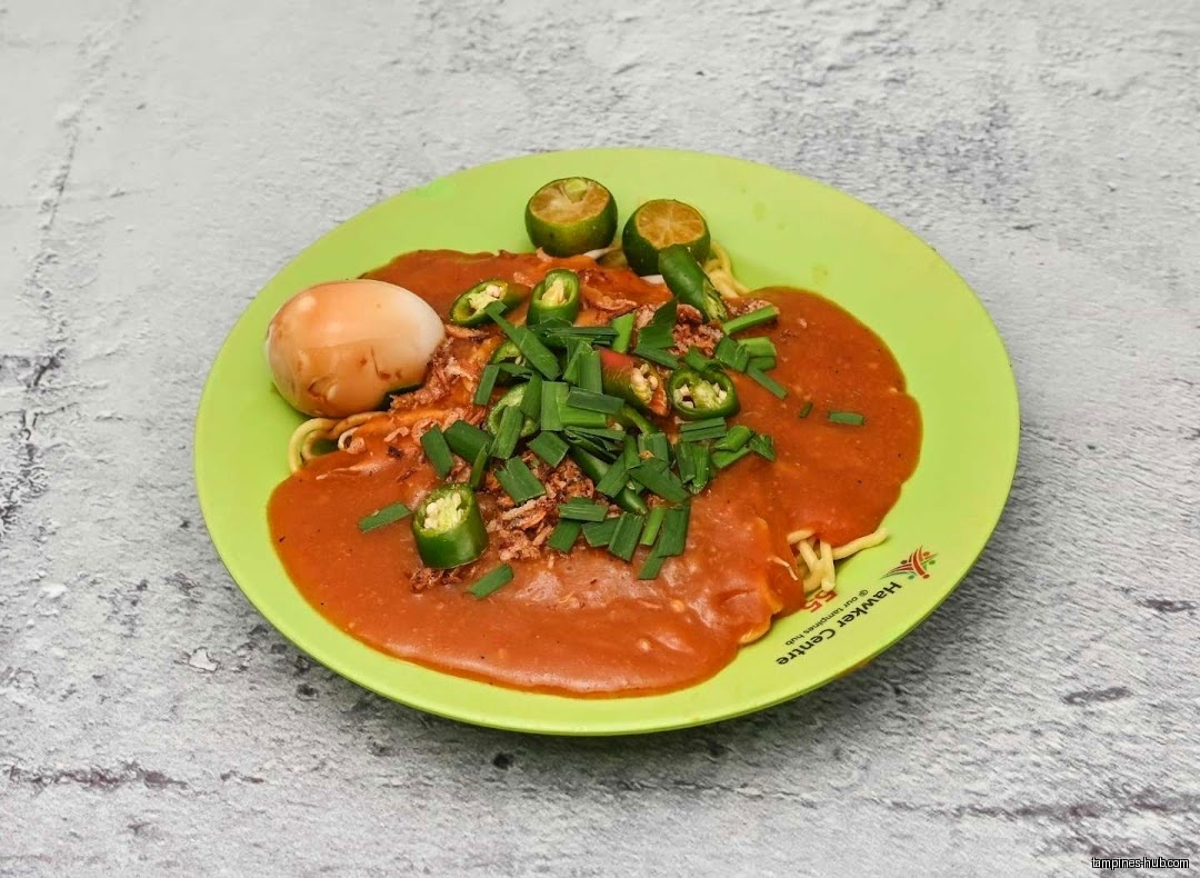 A plate of Mee Rebus with egg, lime, and green chilies.