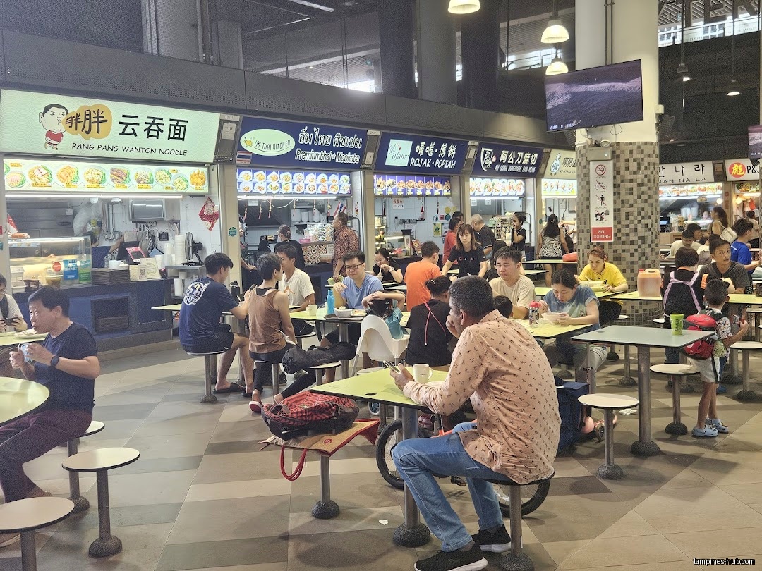 People are eating at tables in a busy food court area.