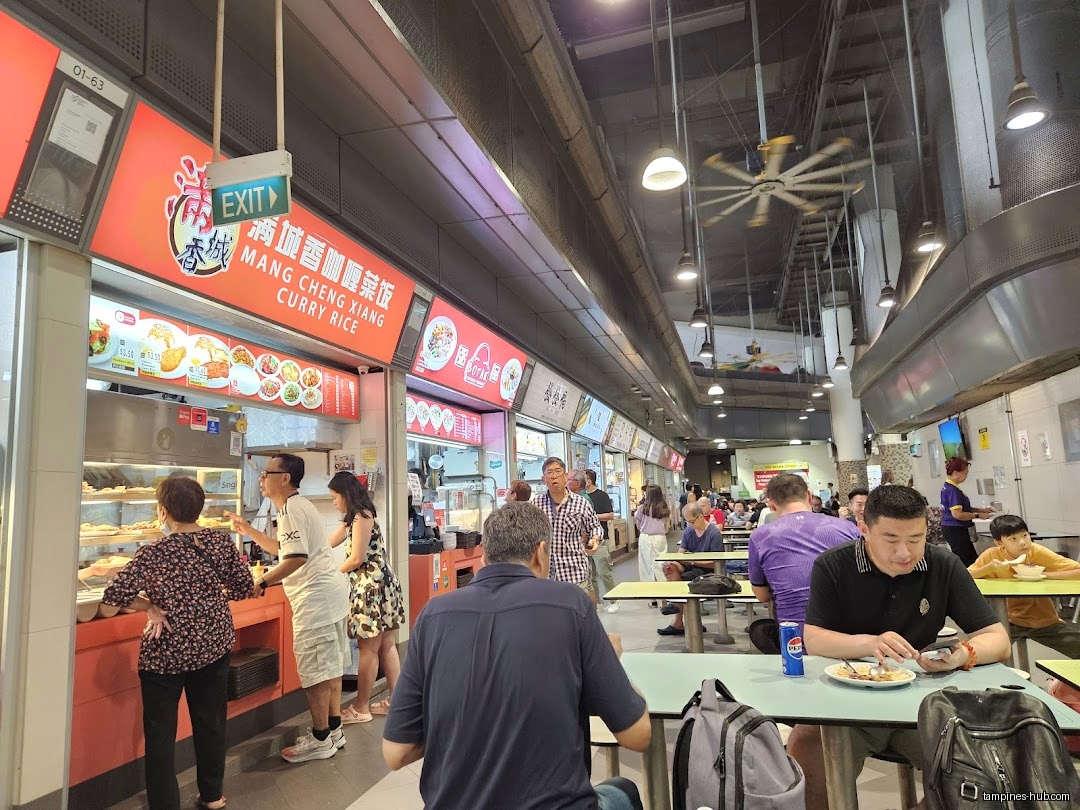 The image shows a busy hawker center with various food stalls and diners.