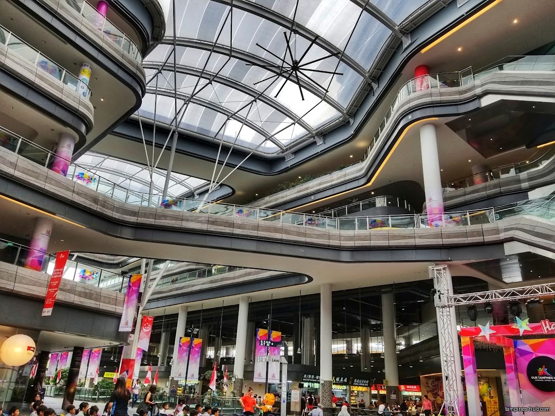 The image shows the interior of a multi-level shopping mall with a glass roof.