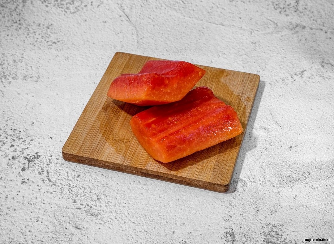 Two pieces of papaya are on a small wooden cutting board.