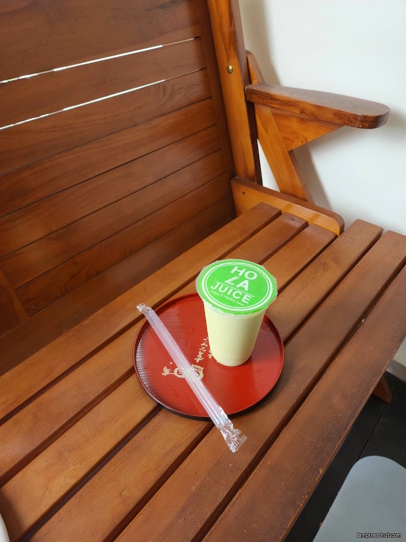 Holla Juice drink on a red tray with straw, sitting on wooden bench.