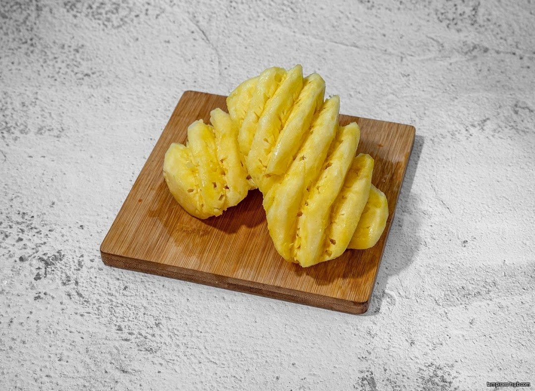 Peeled and sliced pineapple on a small wooden cutting board.