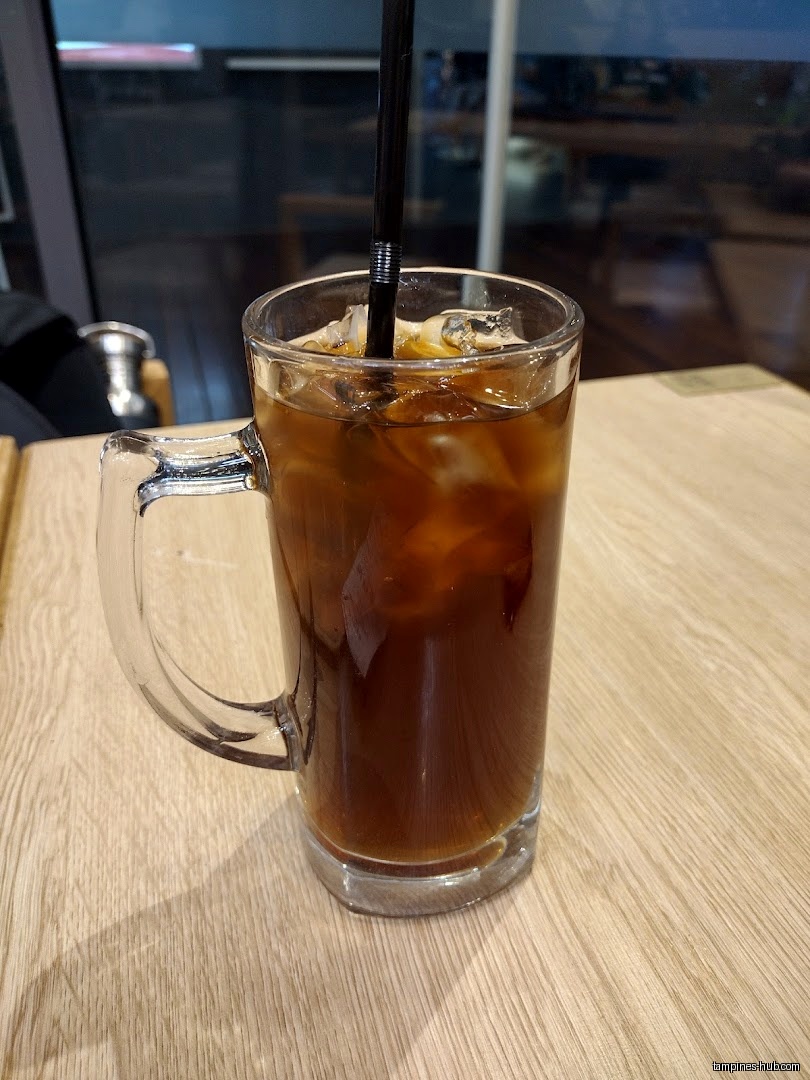 A glass mug filled with iced coffee and a straw sits on a table.