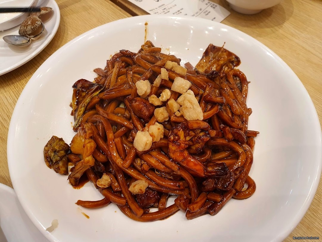 A plate of dark noodles with shrimp and other toppings is shown.