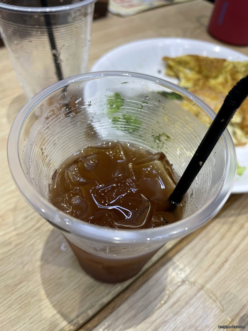 A plastic cup with iced tea and a straw sits on a table.