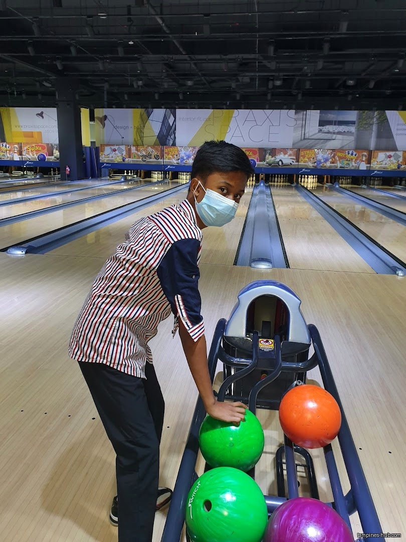 A boy wearing a mask is at a bowling alley with bowling balls.