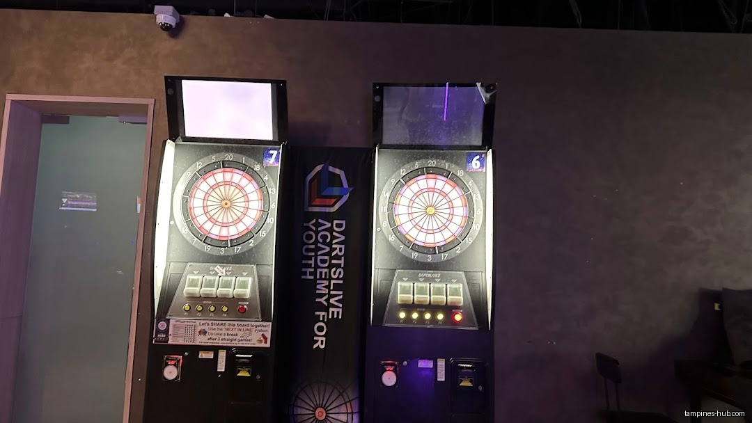 Two electronic dartboards stand side-by-side in a dimly lit room.