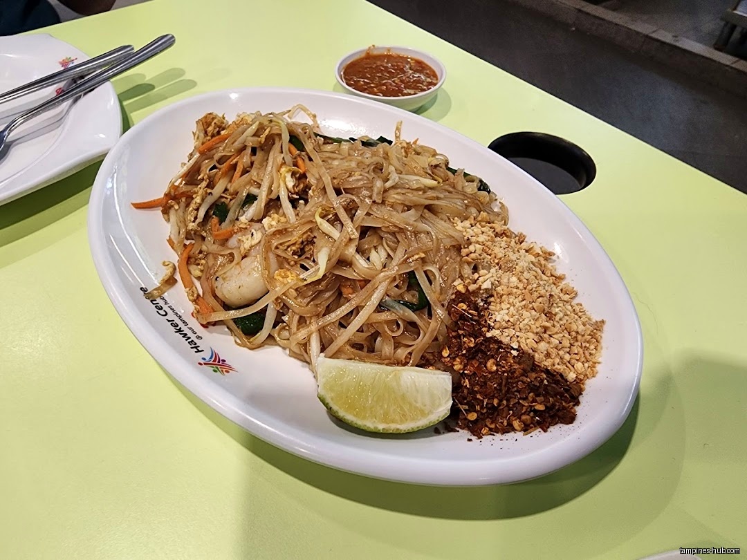 A plate of Pad Thai with peanuts, chili flakes, and a lime wedge.