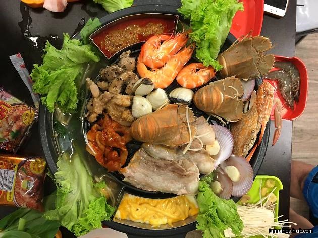 A hot pot with seafood, meat, vegetables, and noodles is shown.