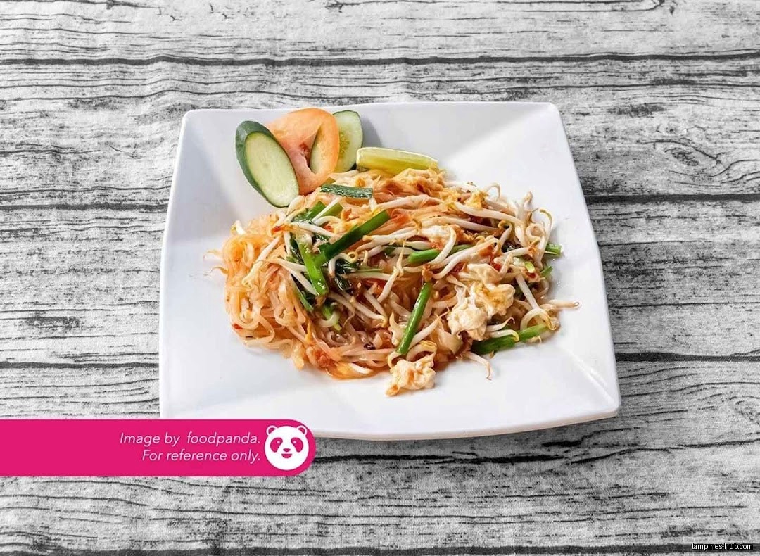 A plate of Pad Thai with vegetables and lime on a table.