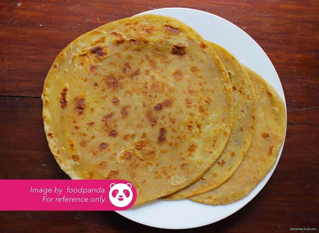 Three paratha breads are stacked on a white plate on a wooden surface.
