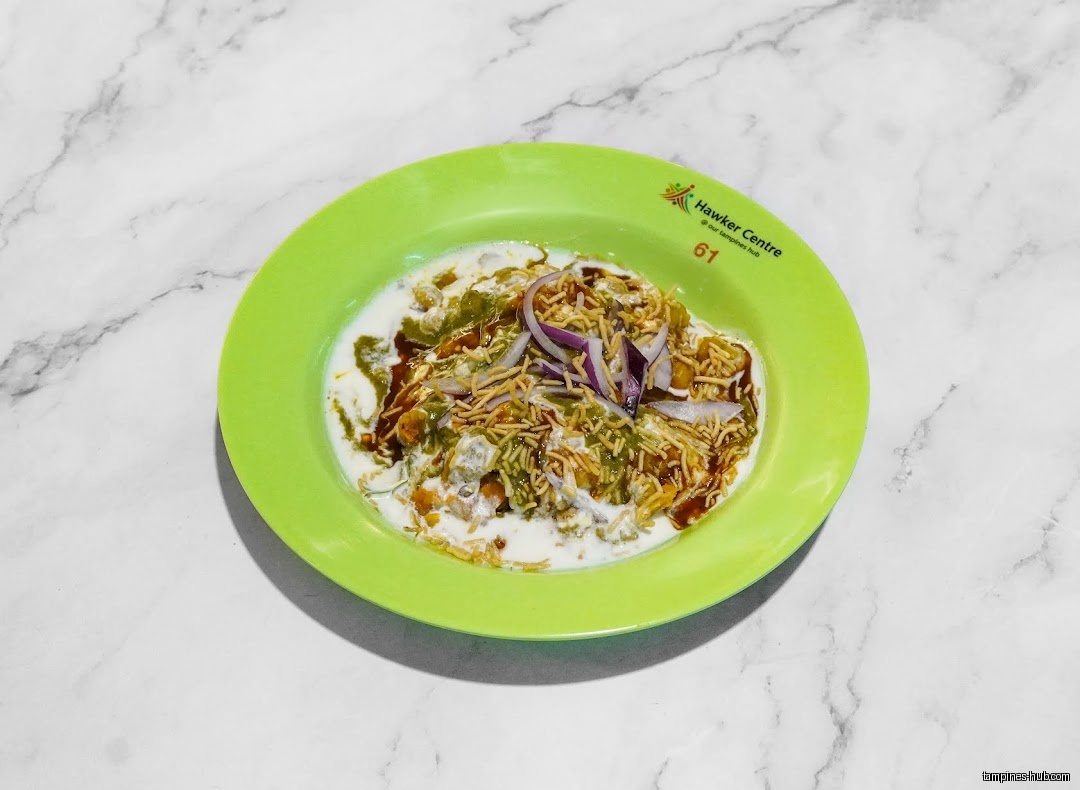 A green plate holds Indian cuisine with yogurt, onions, and spices.