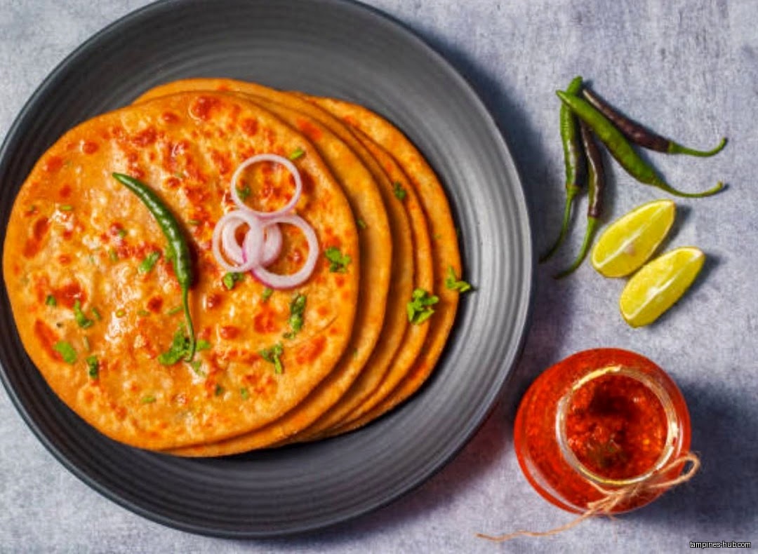 A plate of paratha with chili, onion, lemon and a jar of chutney.