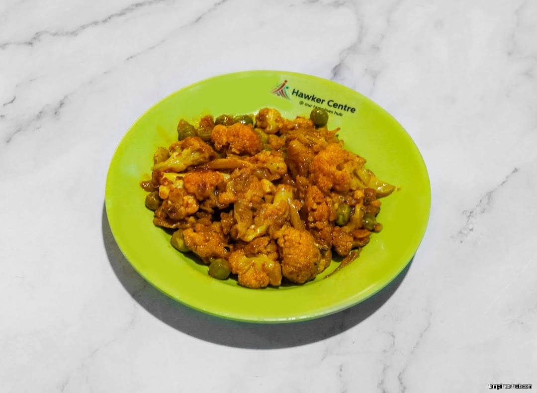 A plate of cauliflower curry with peas on a green plate.