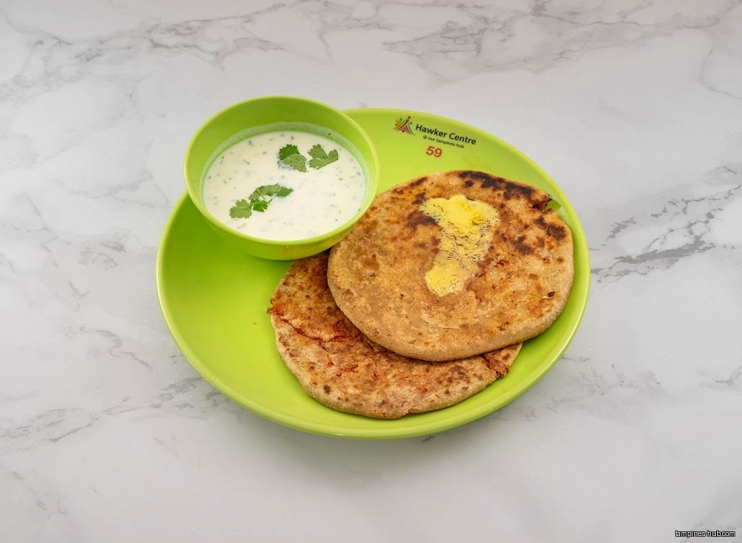 Two parathas with butter and a bowl of raita on a green plate.