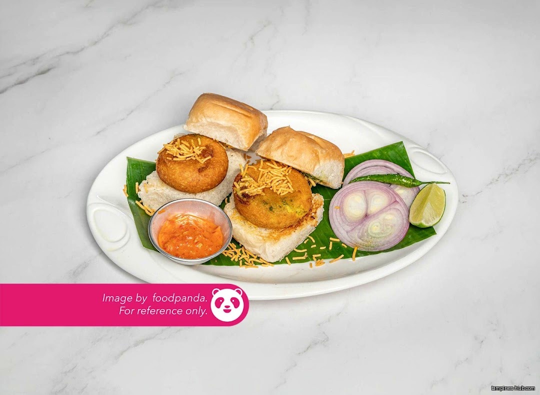 A plate of Indian vada pav with onions, chili, and chutney.