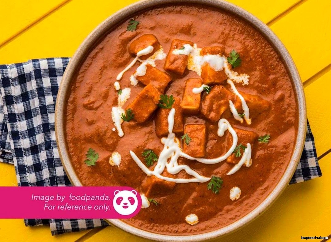 A bowl of paneer butter masala with cream and cilantro garnish.