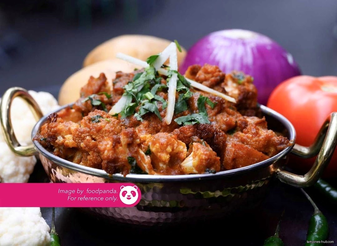A bowl of Indian cauliflower dish with vegetables in the background.