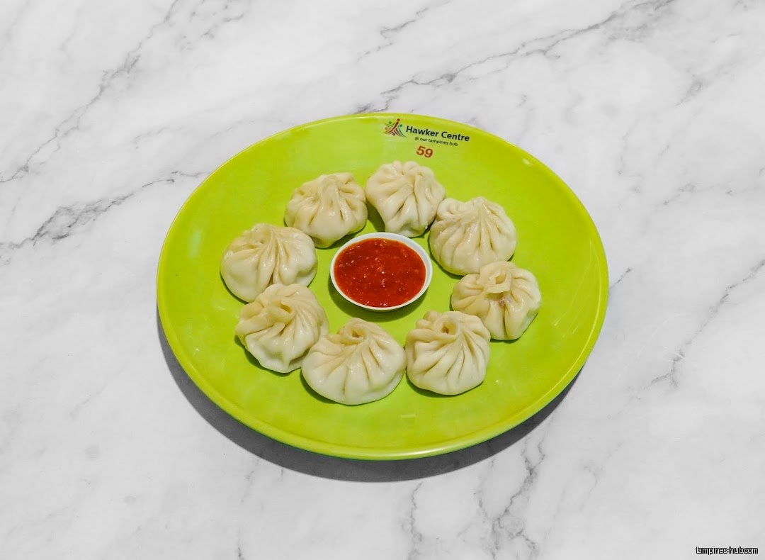 A green plate holds eight dumplings and a small bowl of red sauce.