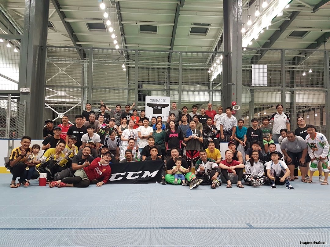 A large group of people pose for a photo at an inline hockey court.