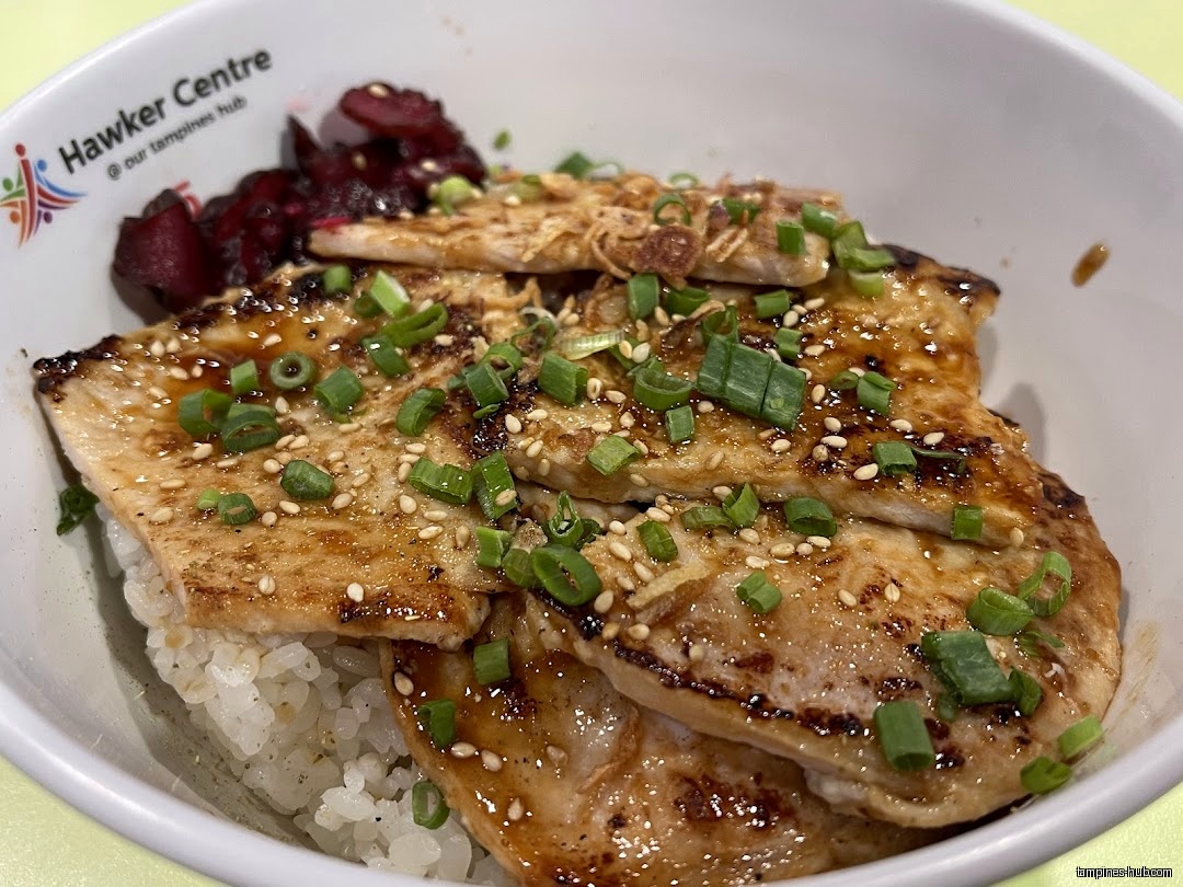 A close-up of a rice bowl topped with meat and garnish.