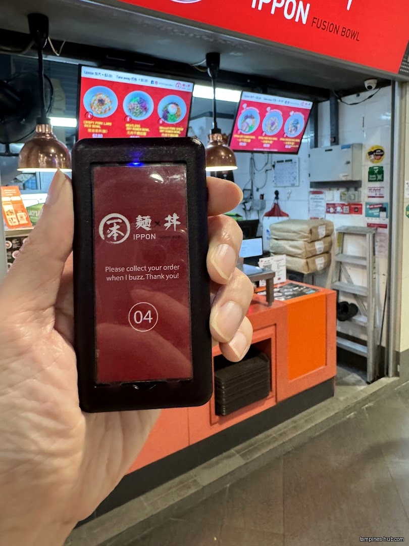 Hand holding a buzzer from IPPON Fusion Bowl with shop background.