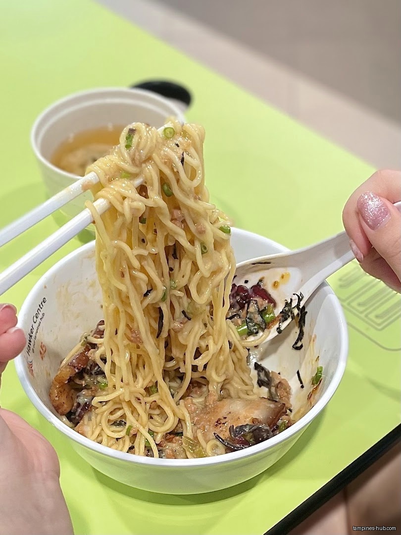A bowl of noodles being lifted with chopsticks and a spoon.