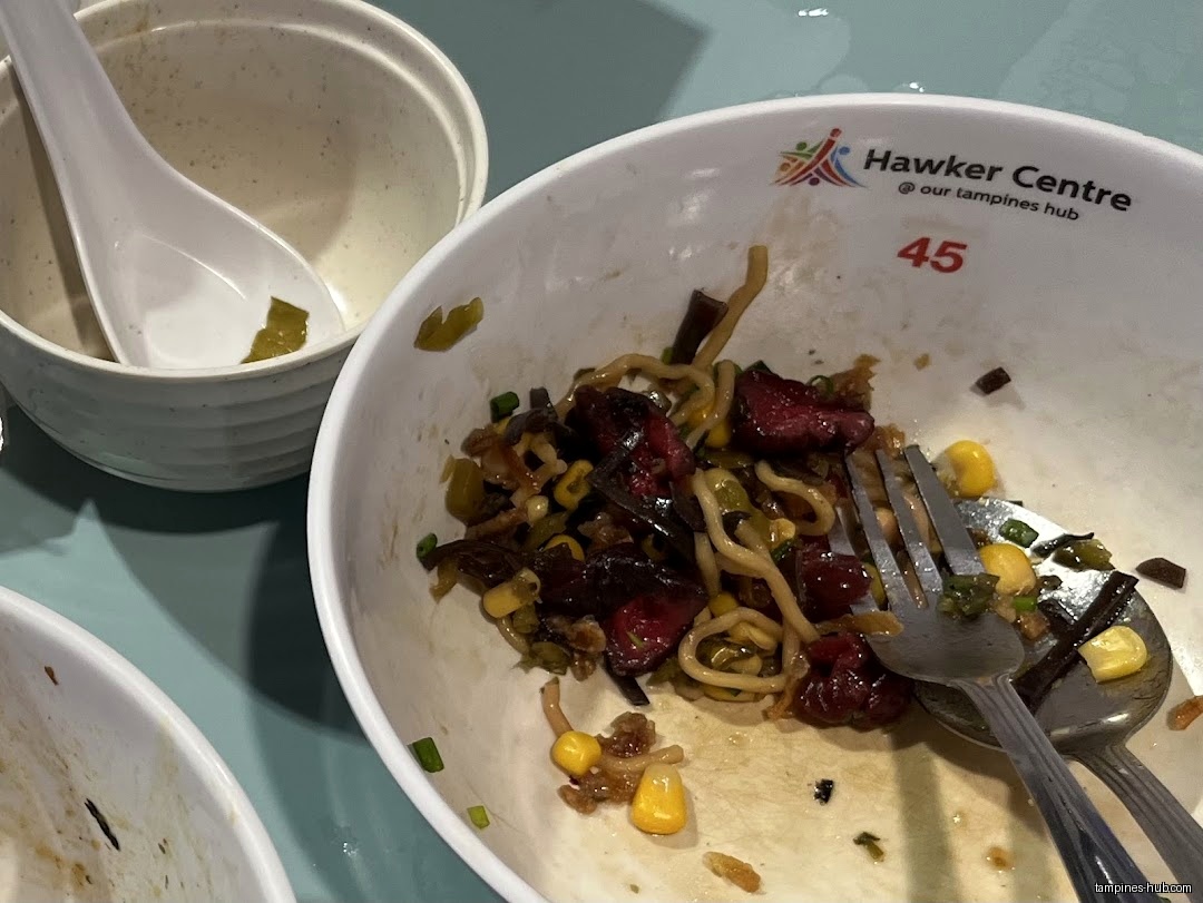 Close-up of a nearly empty bowl of noodles with corn and meat.