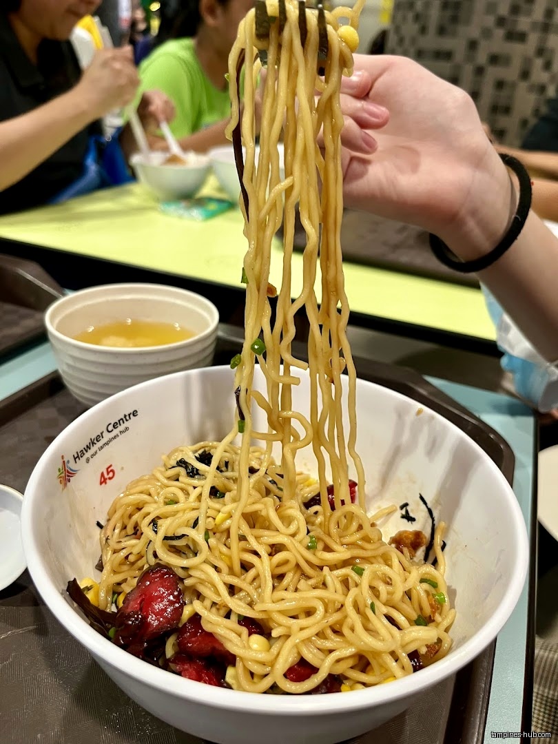 A bowl of noodles with meat and vegetables is being lifted with chopsticks.