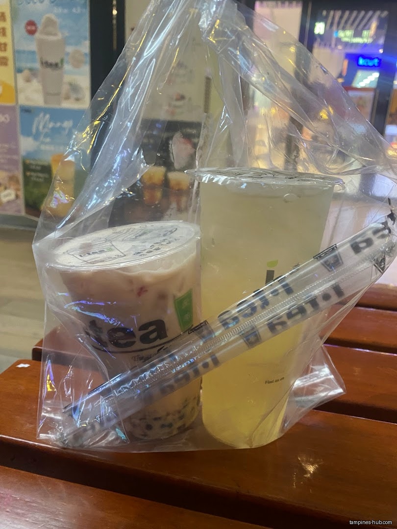 Two iTEA drinks in a plastic bag with straws on a table.