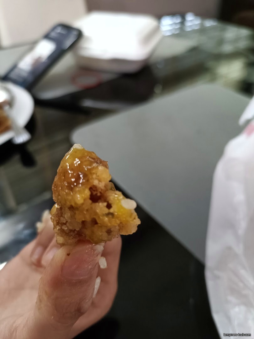 A hand holds a piece of fried food with a glossy sauce.