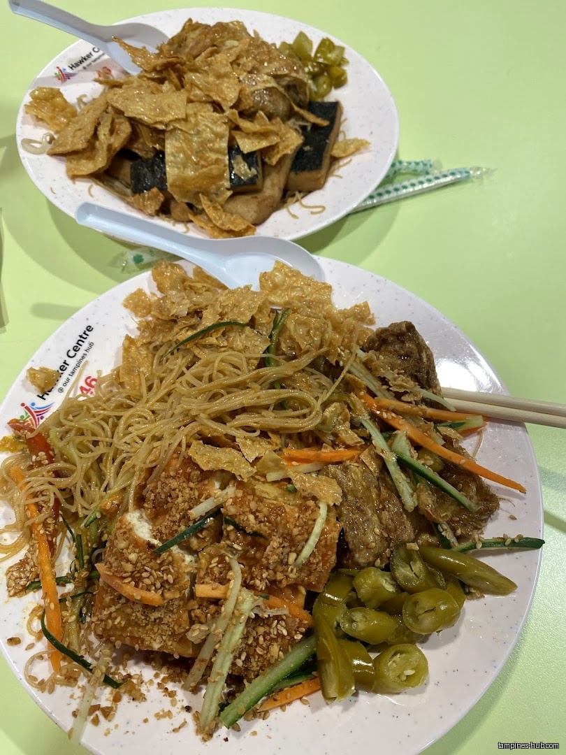 Two plates of vegetarian food with tofu, noodles, and vegetables are shown.