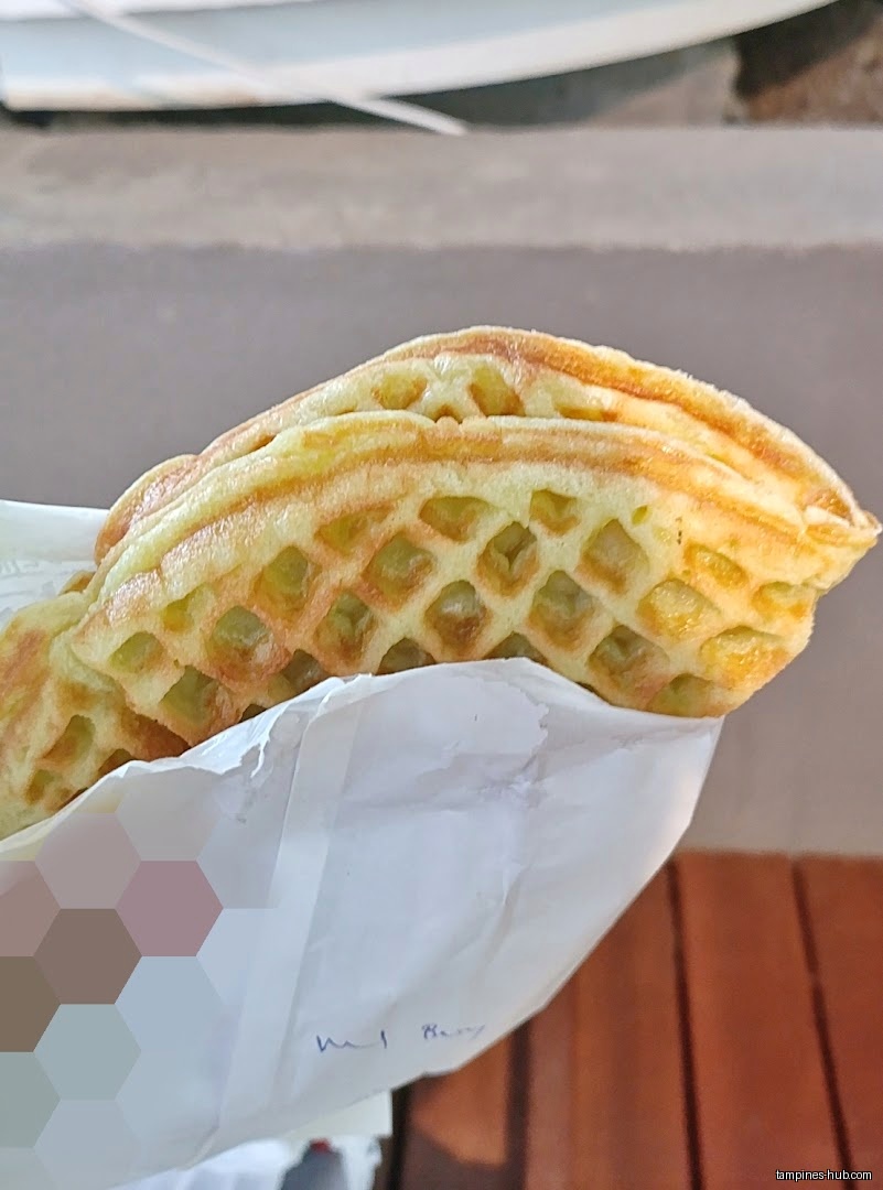 A waffle from KenJinn Bakery is held in a white paper bag.