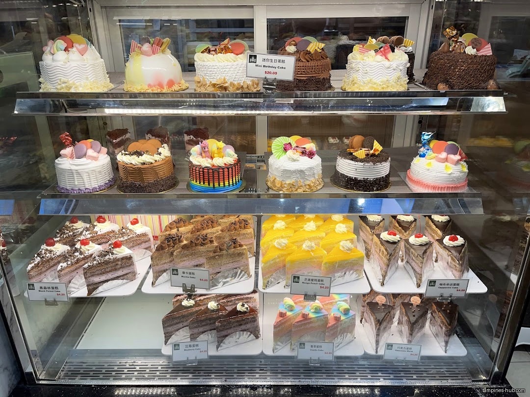 A display case filled with various cakes and slices at KenJinn Bakery.