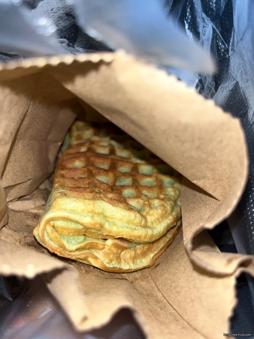 A waffle is inside a brown paper bag, possibly from KenJinn Bakery.
