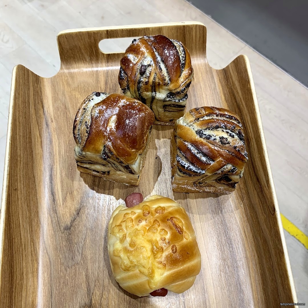 A wooden tray holds three chocolate pastries and one sausage bun.